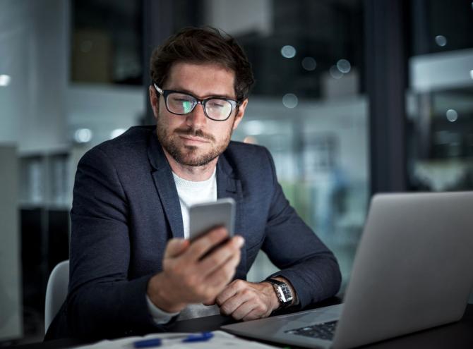 Businessman with laptop looking at mobile phone