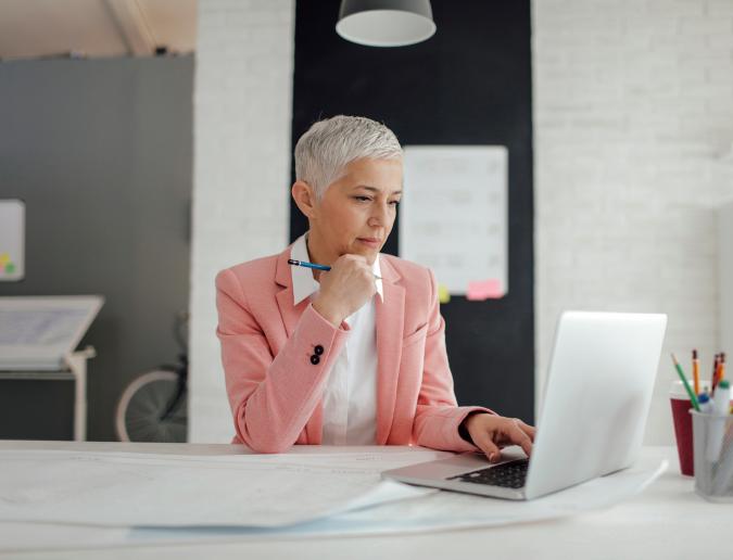 Older businesswoman sitting at desk in front of a laptop in an office